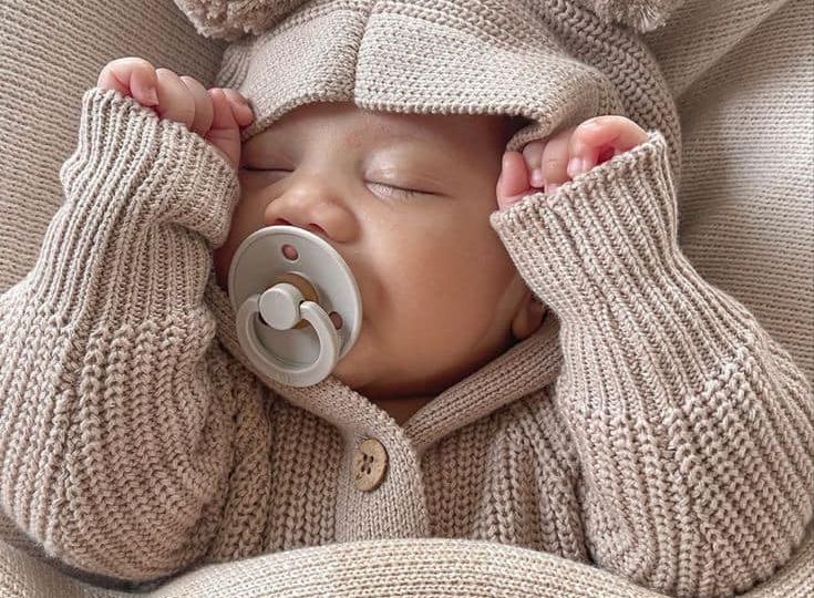 Sleeping baby in cut winter outfit, covered with blanket.